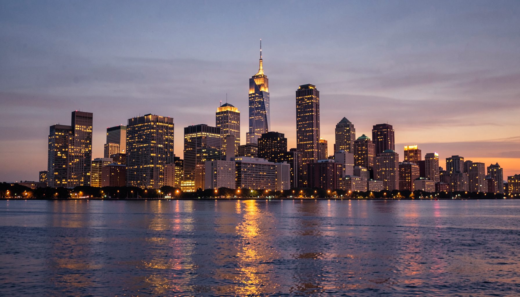 Chicago skyline at dusk with warm amber lights reflecting off Lake Michigan, urban and inviting mood